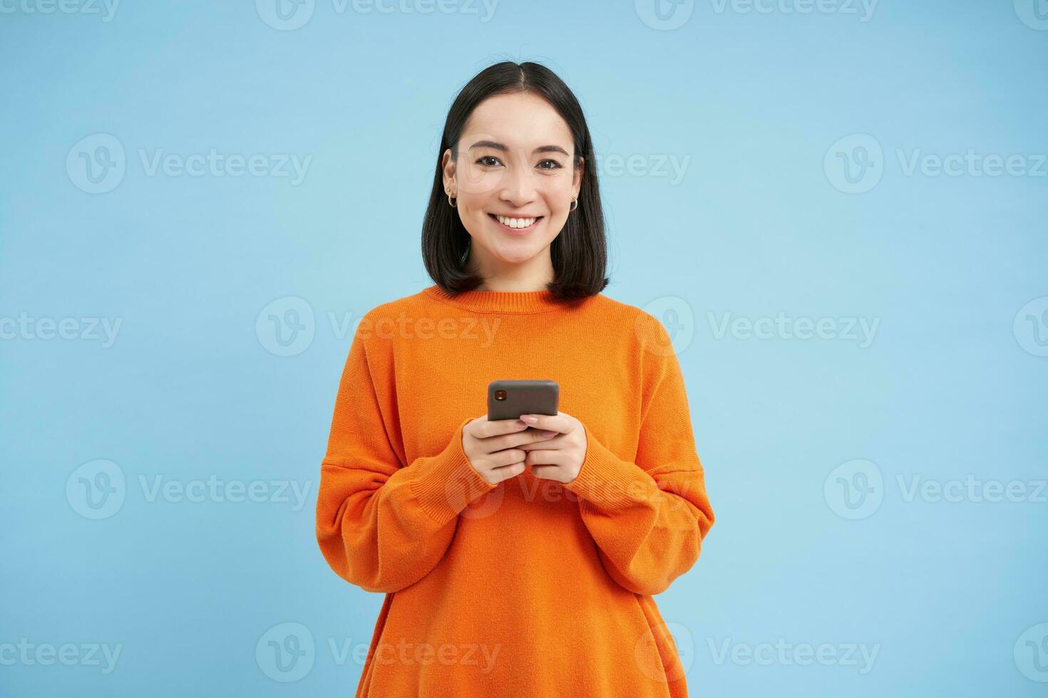 Girl with smartphone in hands smiling, using mobile application on her phone, sending message or order something online, blue background photo