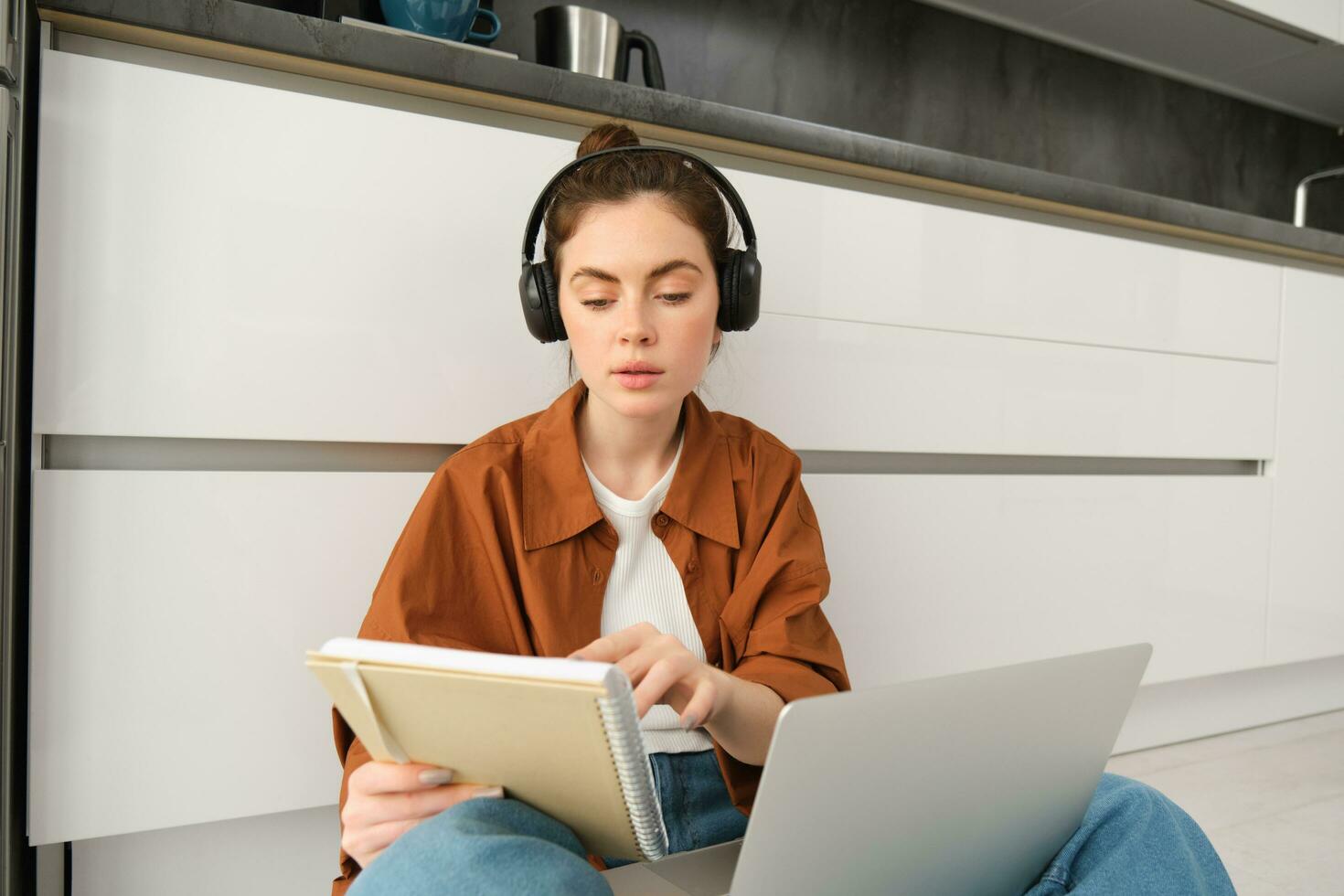 Concentrated young student, woman working on assignment, doing homework on laptop, making notes in notebook during online lesson, remote college course photo