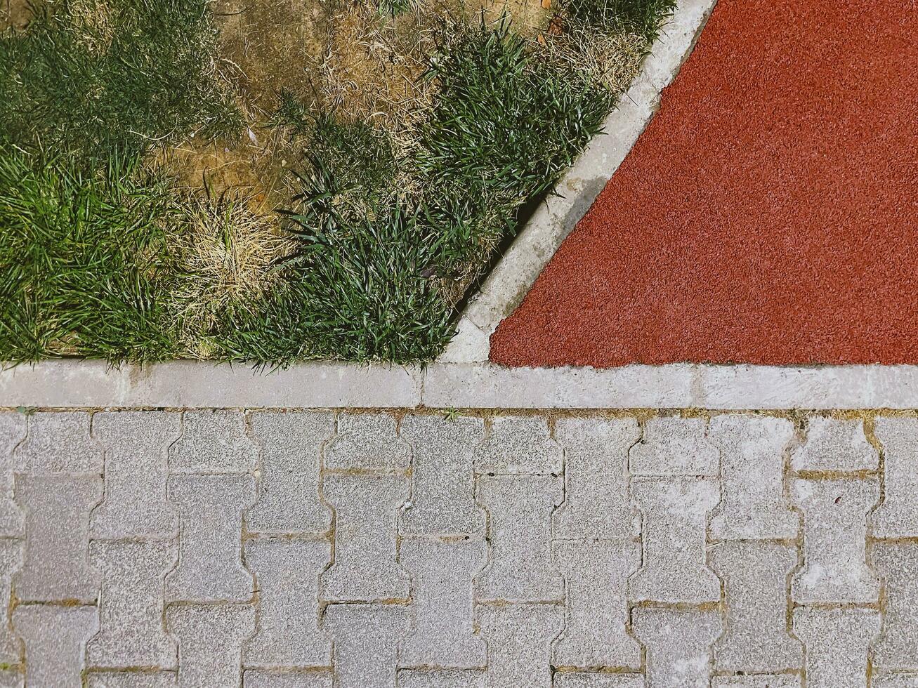 A contrasting view of green grass, withering turf, a red athletic track, and grey paving stones, depicting varied textures photo