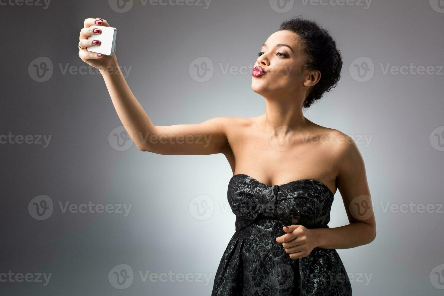 Portrait of a Beautiful successful smiling girl doing selfie in black dress on light background photo