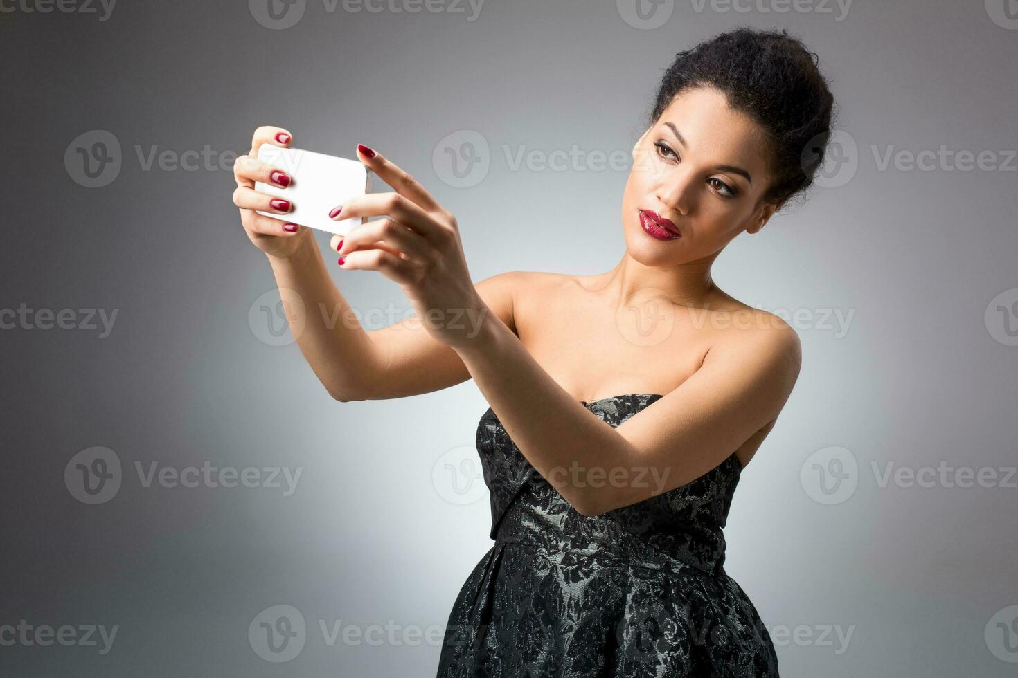 Portrait of a Beautiful successful smiling girl doing selfie in black dress on light background photo