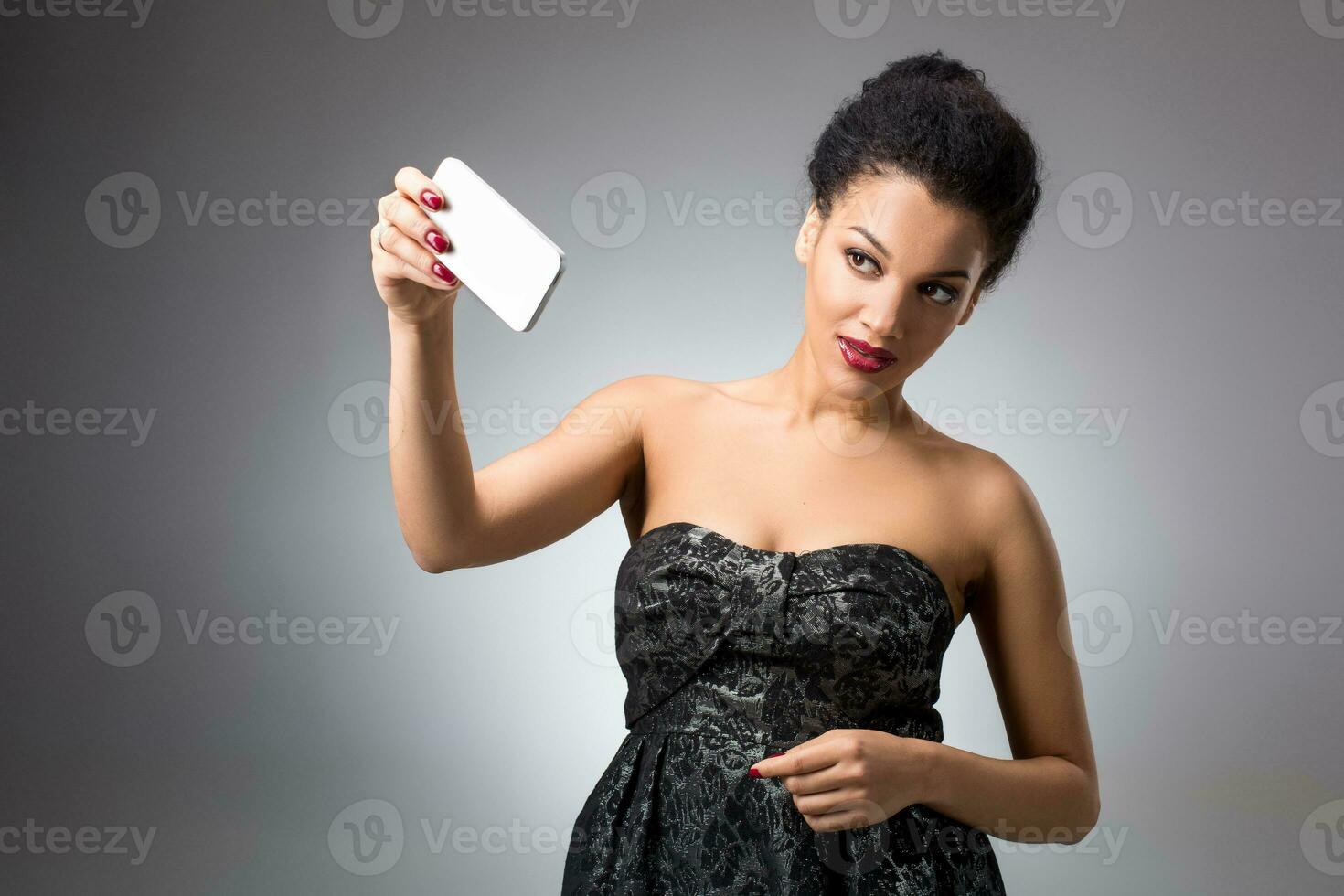 Portrait of a Beautiful successful smiling girl doing selfie in black dress on light background photo