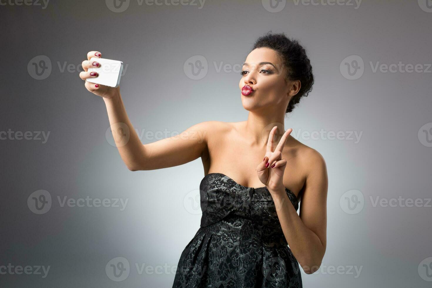 Portrait of a Beautiful successful smiling girl doing selfie in black dress on light background photo