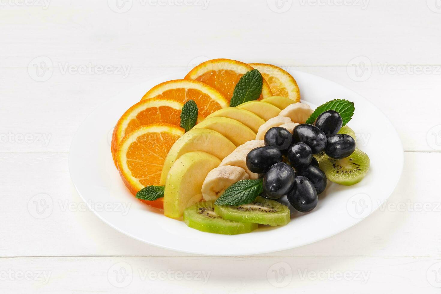 Slices of orange, banana, kiwi, apple and grape on plate photo