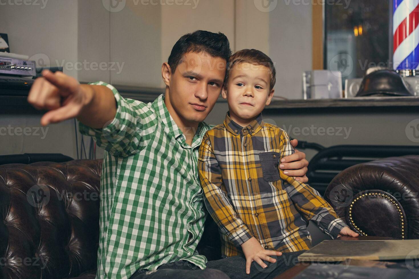 Young father and his stylish little son in the barbershop in the waiting room. photo