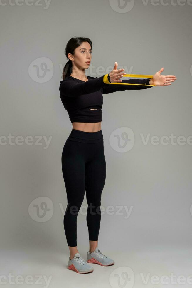 Girl stretching resistance band on outstretched arms on grey background photo