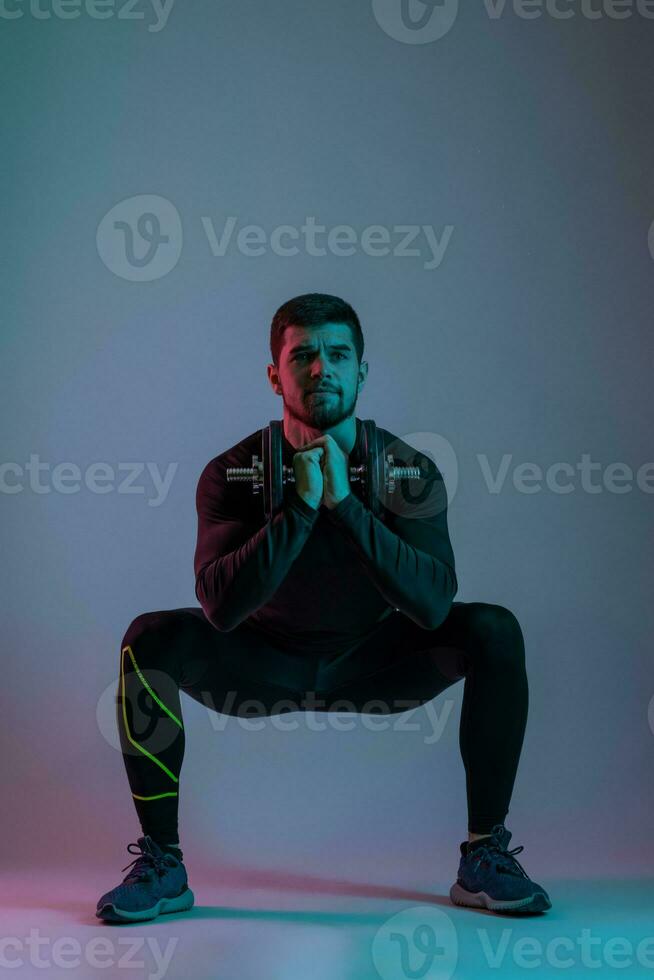 Athletic young man performing dumbbell sumo squats photo