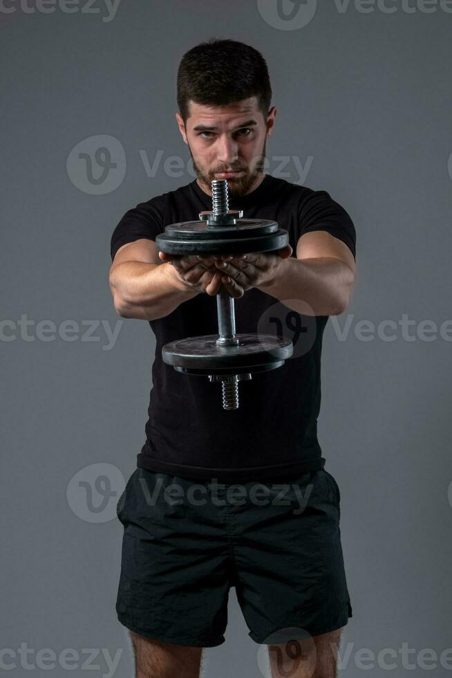 Athletic guy performing one dumbbell front raise photo