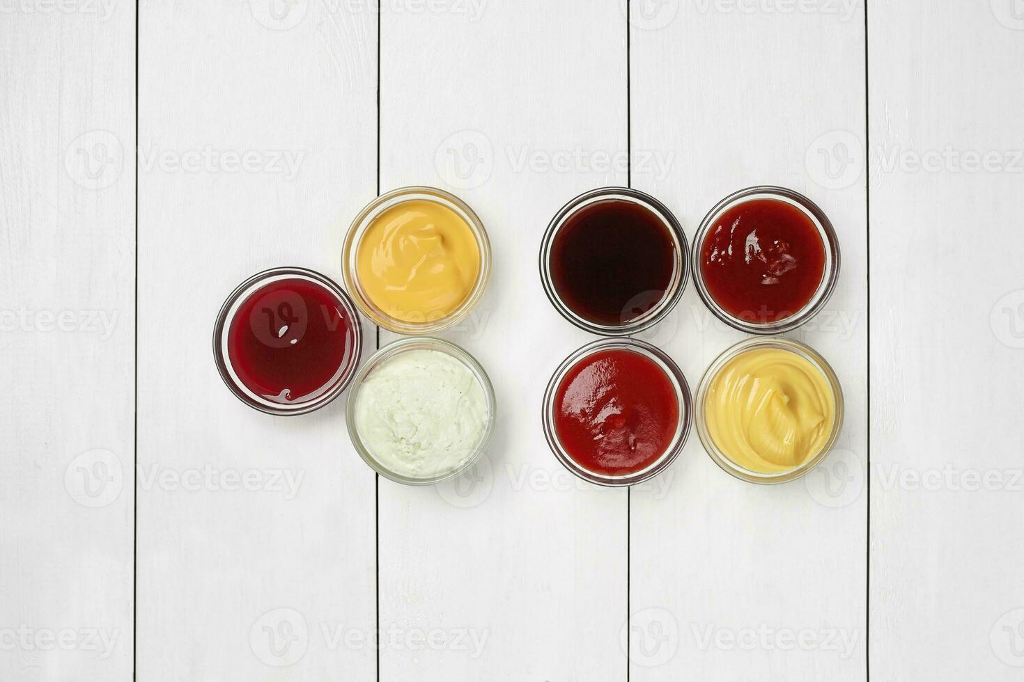 Glass bowls with dipping sauces on white wooden surface photo