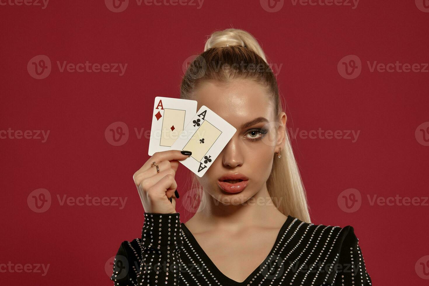 rubia niña en negro vestir en pedrería. demostración dos jugando tarjetas, posando en contra rojo antecedentes. juego entretenimiento, póker, casino. de cerca foto