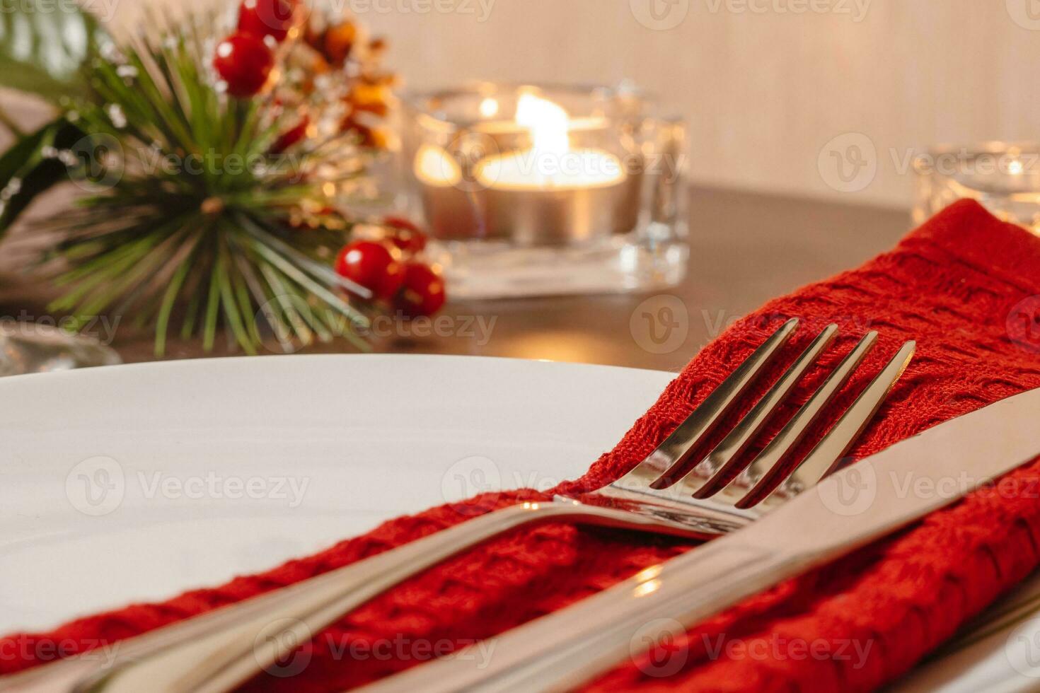 Christmas table setting. Plate and cutlery on napkin. Preparing for festive dinner. Candles burning on table on Christmas Eve. photo