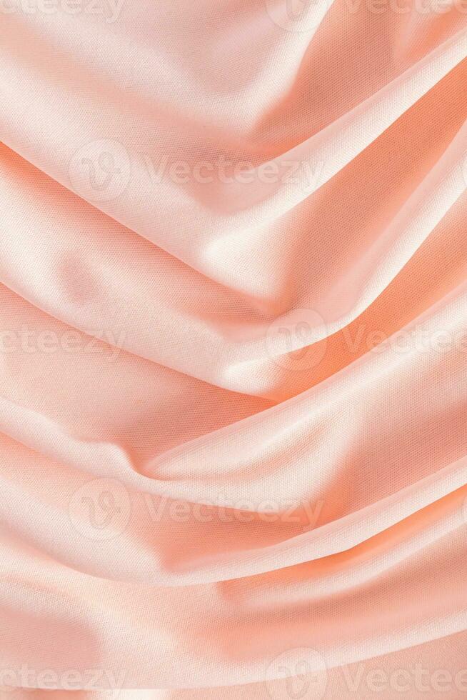 Soft pleats of peach colored satin textiles. Luxury abstract textile background design. Vertical view. Color of the Year 2024 peachy fuzz. photo