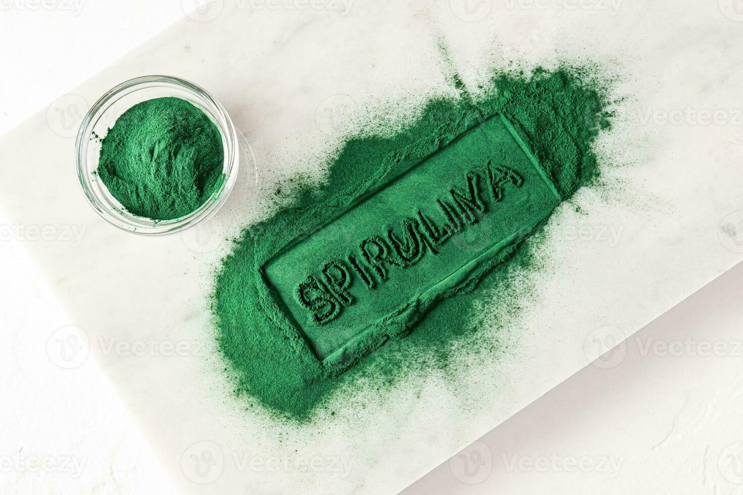 Inscription of green powder of natural spirulina algae on a white slice marble stone with a bowl filled with green powder. Organic super food. photo