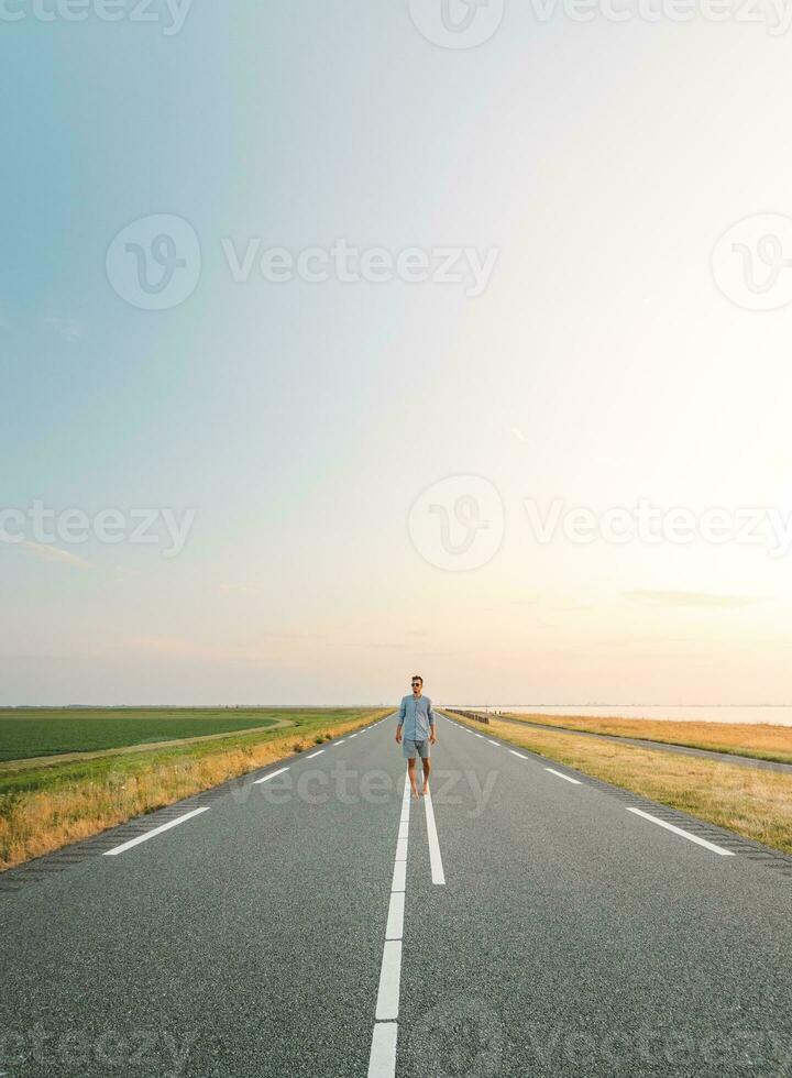 Brown-haired man in a checked shirt walks along a road at sunset on the outskirts of Almere, Netherlands. Fashion lifestyle photo