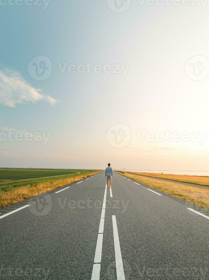 Brown-haired man in a checked shirt walks along a road at sunset on the outskirts of Almere, Netherlands. Fashion lifestyle photo