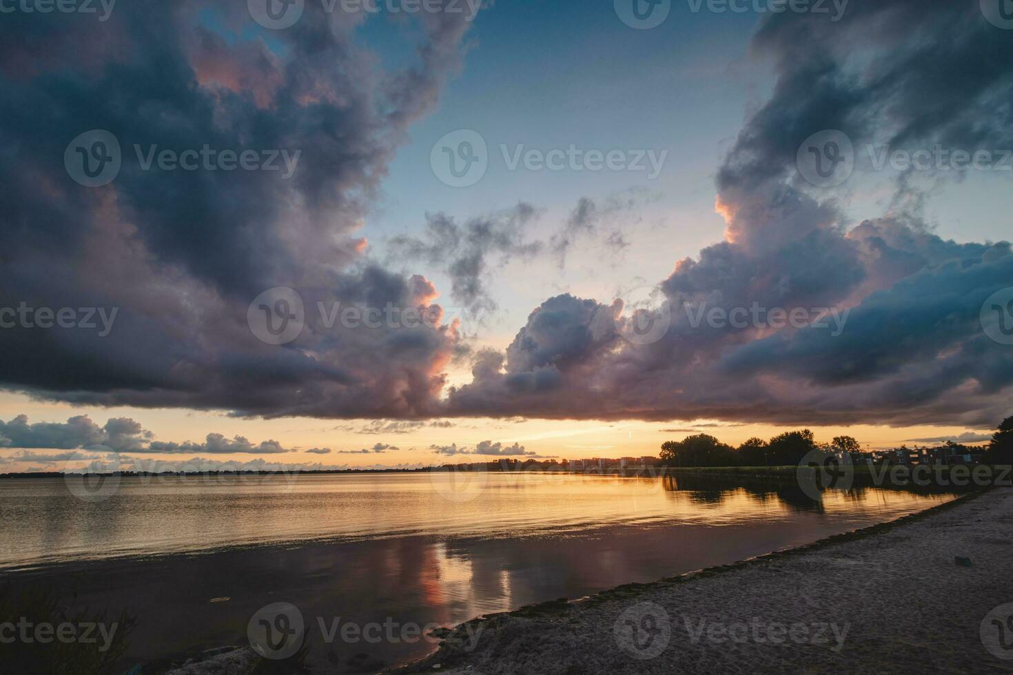 Perfect sunset on the shores of Lake Gooimer near Almere. The purple-orange inferno illuminates the passing clouds and reflects on the calm surface. Beauty of Netherlands photo