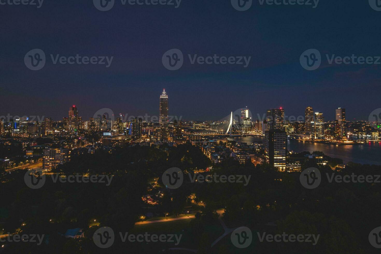 Night aerial view of the sleepless city of Rotterdam and architectural buildings. Glowing skyscrapers and the famous Erasmusbrug bridge. The modern city of the Netherlands photo