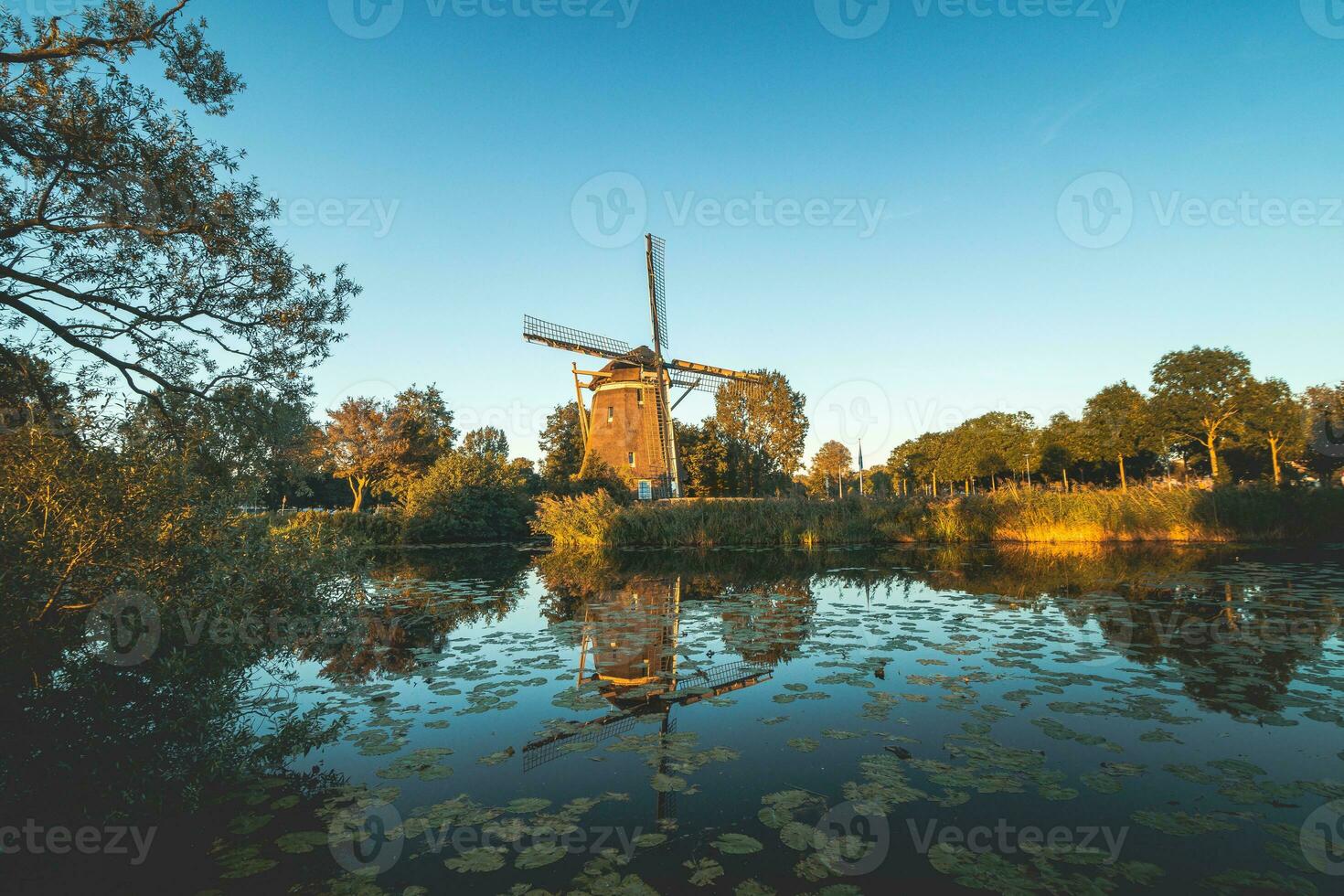 Last rays of the sun shine on an ancient wooden windmill on the banks of a river in Amsterdam, the Netherlands photo