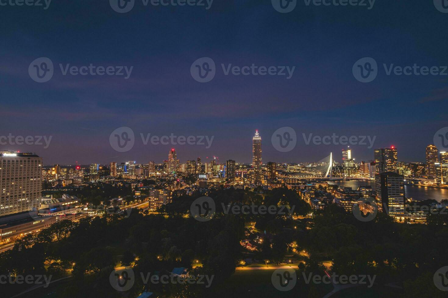 Night aerial view of the sleepless city of Rotterdam and architectural buildings. Glowing skyscrapers and the famous Erasmusbrug bridge. The modern city of the Netherlands photo