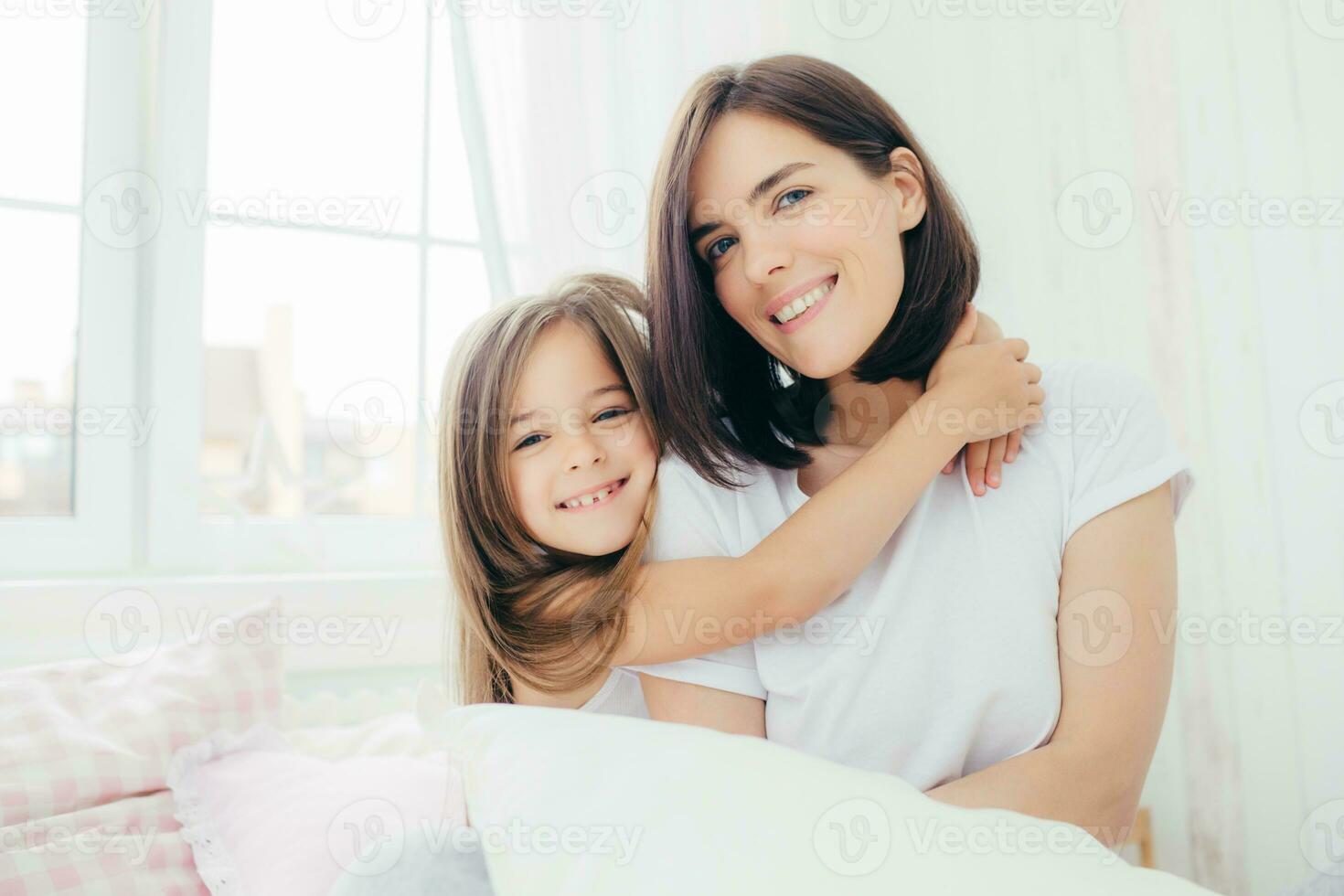 Mother and daughter sharing a joyful hug, smiling in a bright room photo