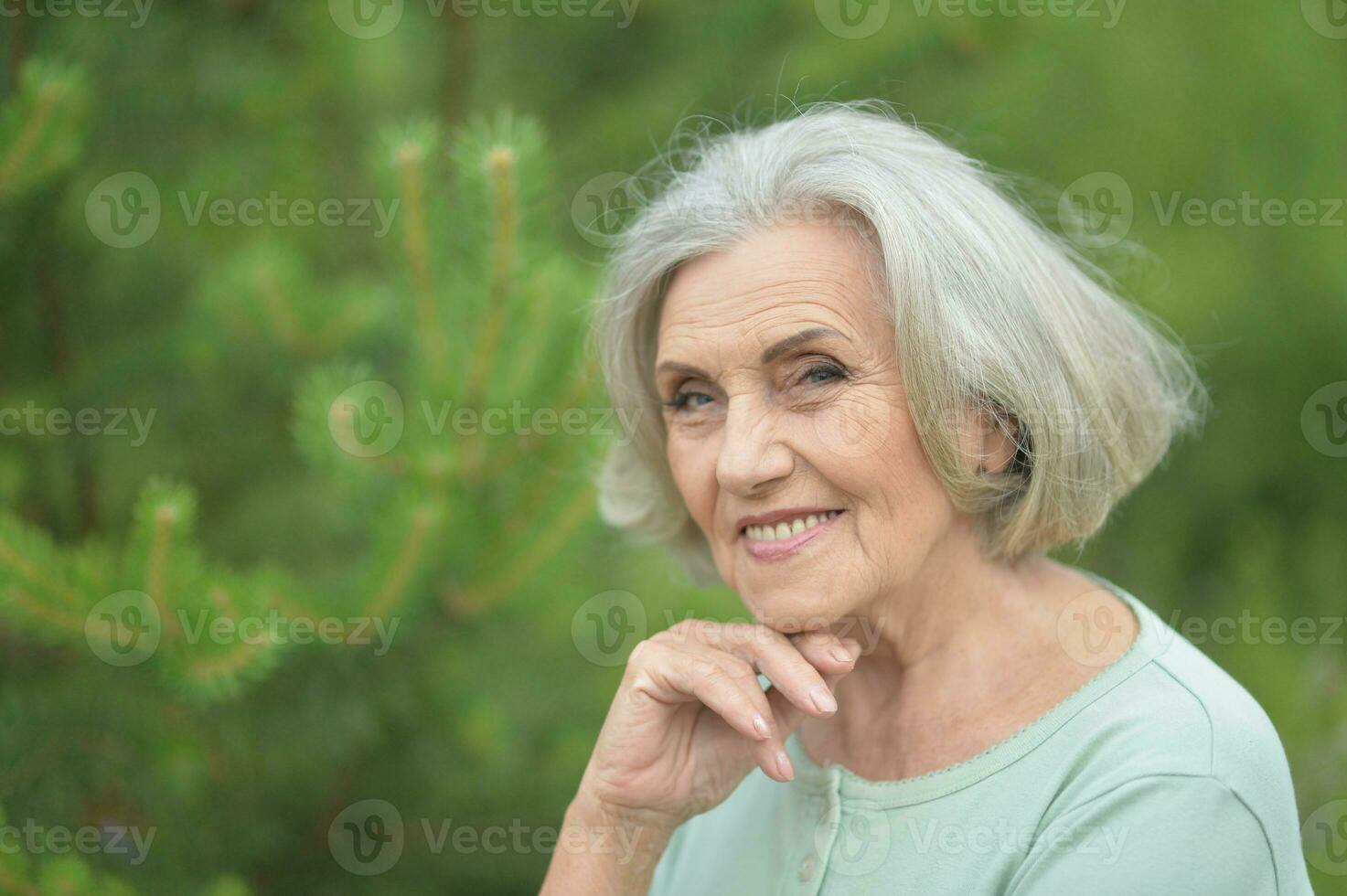 Closeup portrait of smiling elderly woman posing in summer park photo