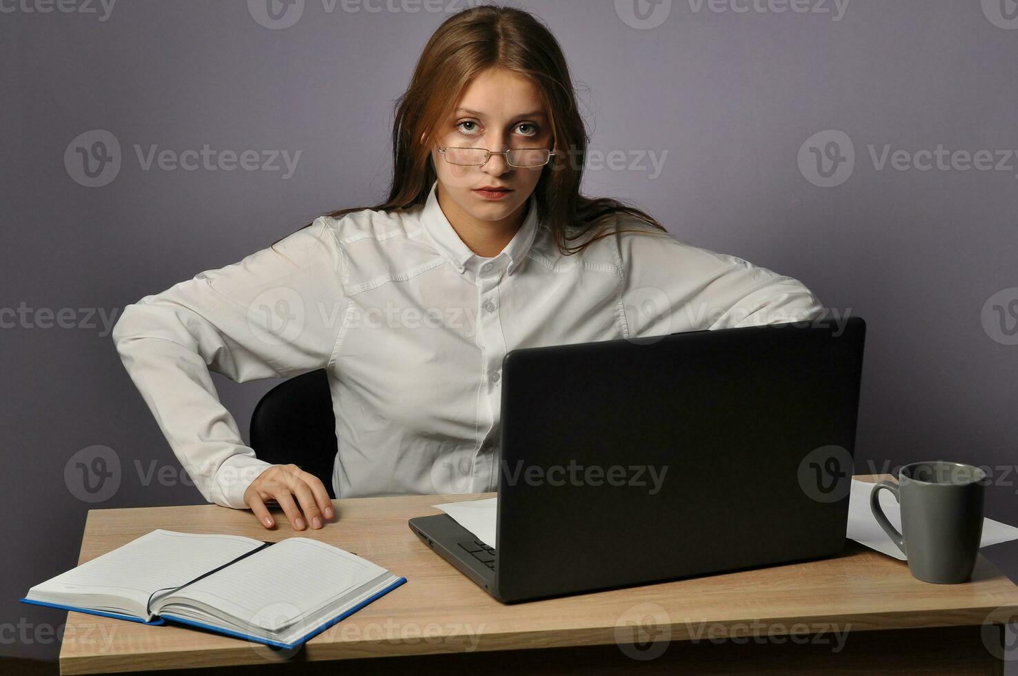 Portrait of an angry business woman sitting near the table and looking at the camera. Grumpiness and work concept photo