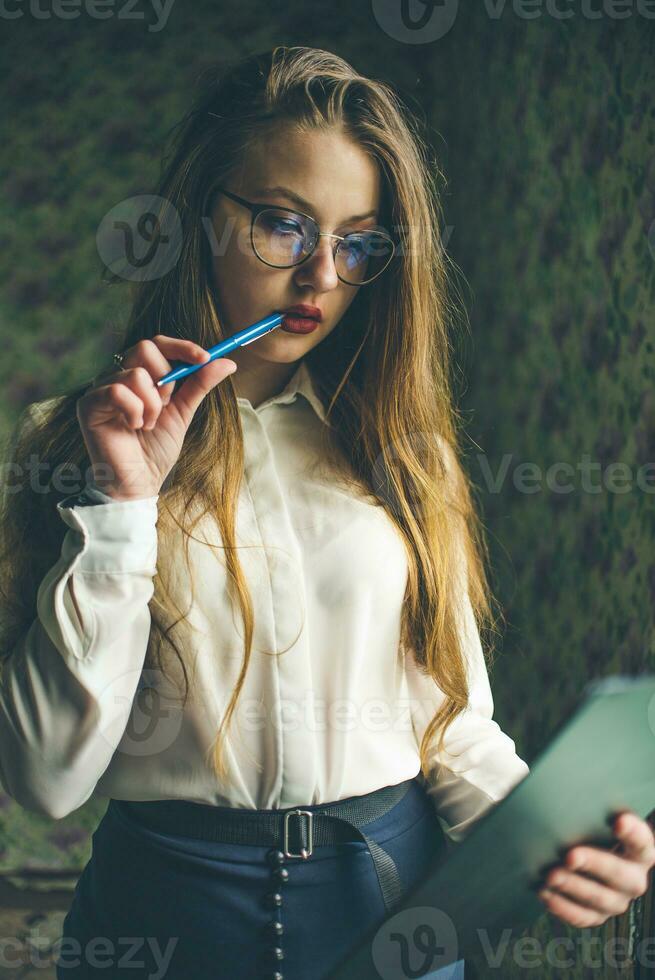 A girl in business clothes and glasses holds a black folder in her hands. photo