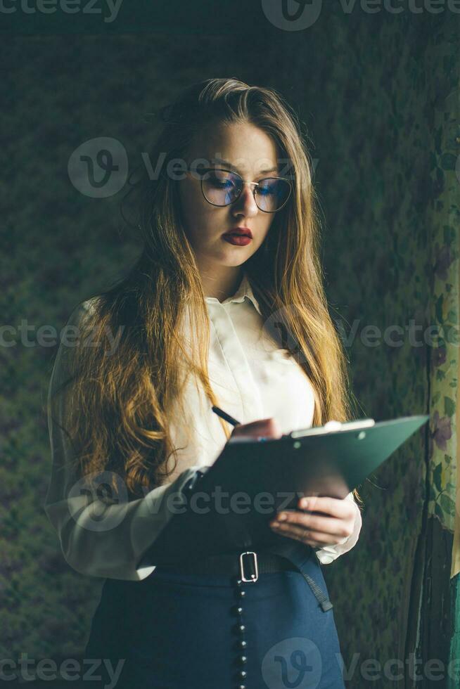 A girl in business clothes and glasses holds a black folder in her hands. photo