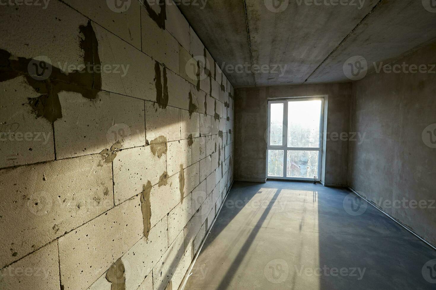 Unfinished empty room with plastic window, walls made of aerated concrete blocks and cement screed on the floor in a building under construction photo