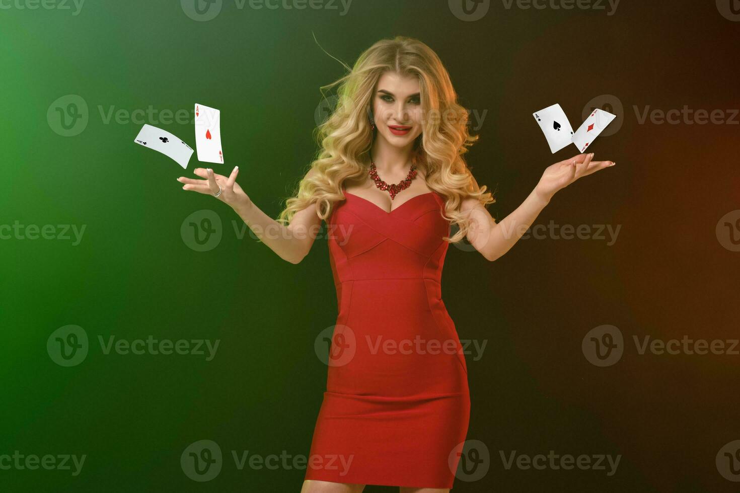 Blonde model, bright make-up, in red fitting dress and necklace. Holding or throwing something, posing on colorful background. Copy space, close up photo