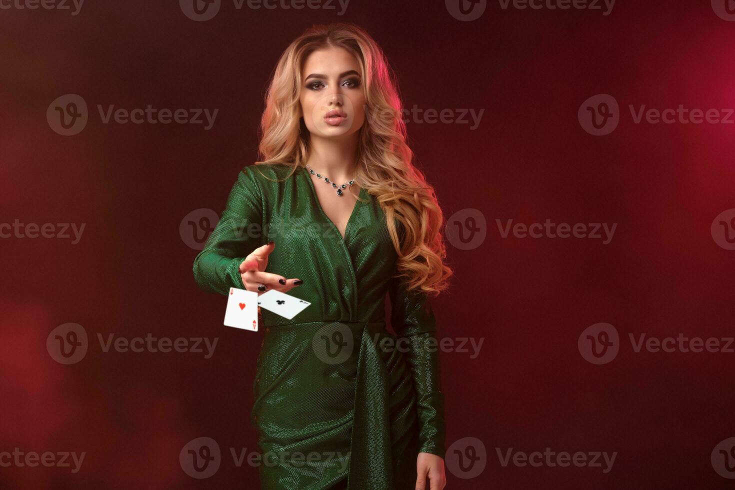 Blonde model, bright make-up, in green dress and jewelry. Holding something, throwing it, posing on colorful smoky background. Copy space, close up photo