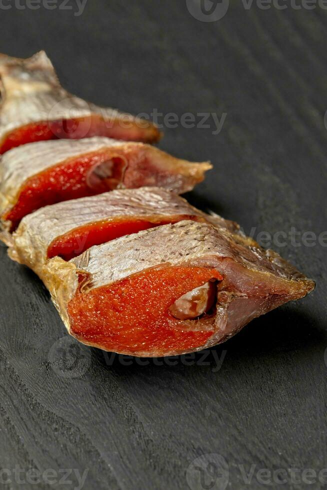 Slices of salted air-dried roach with roe on black wooden table photo