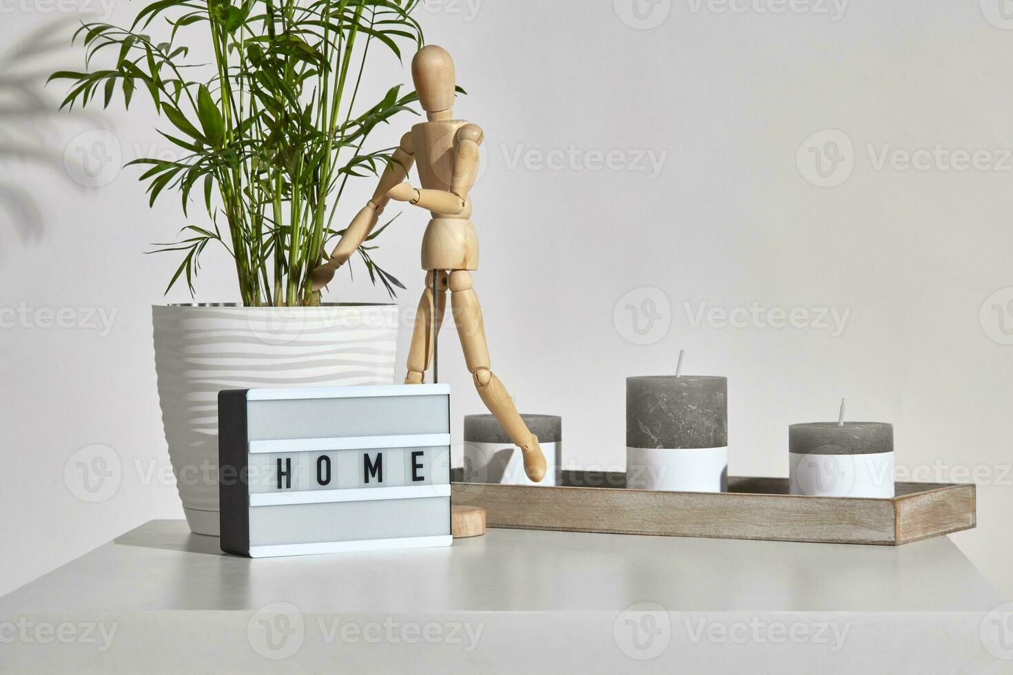 Table, gray different sized candles on wooden stand, figurine of human, lamp with inscription home, green plant in pot. Isolated on white. Close up photo