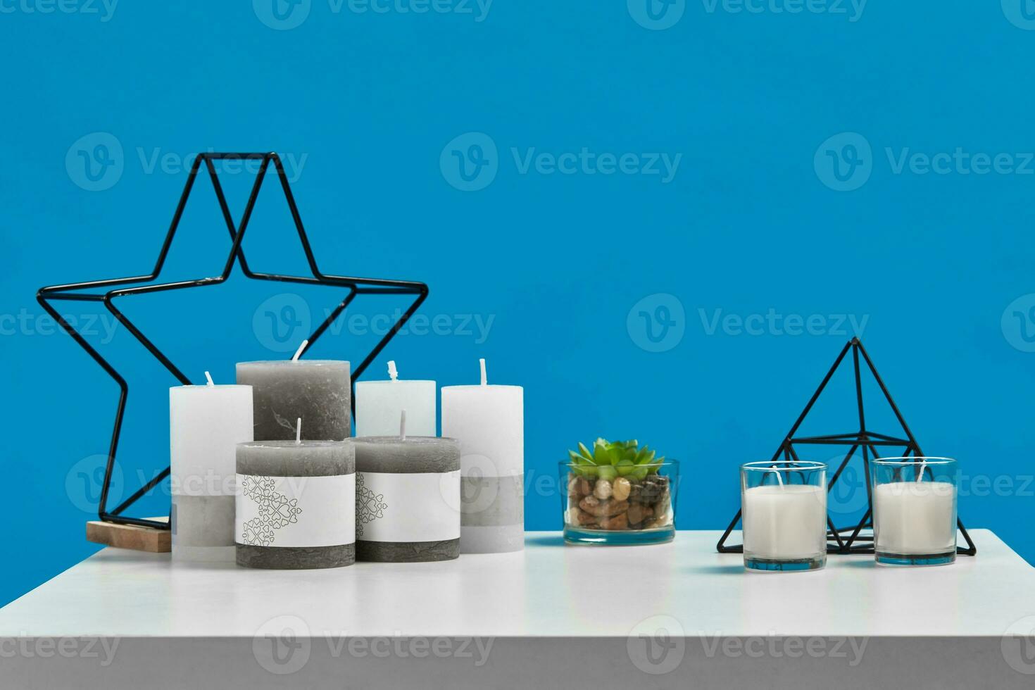 White table with green succulent in glass pot, some candles with copy space, iron star on wooden stand, black triangle. Blue background. Close up photo