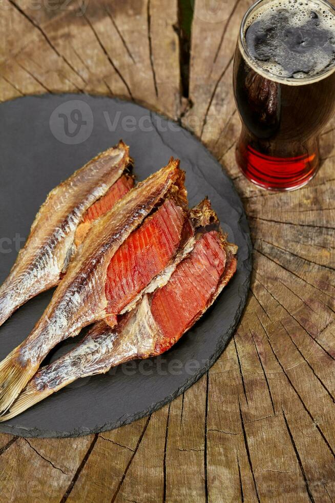 Skinned sun-dried roach with roe and glass of beer on wooden background photo