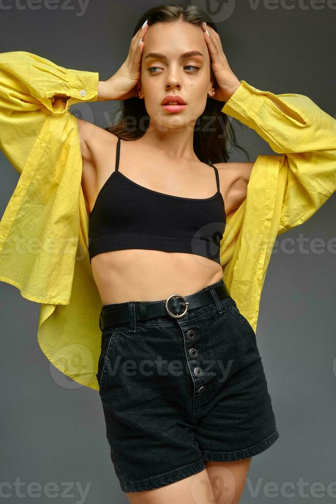 Young woman in yellow shirt posing on grey background photo