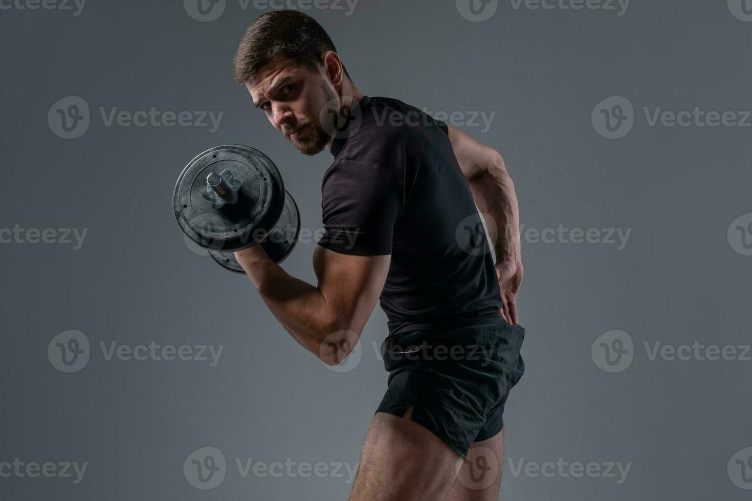 Muscular young bodybuilder doing bicep curl with dumbbell photo