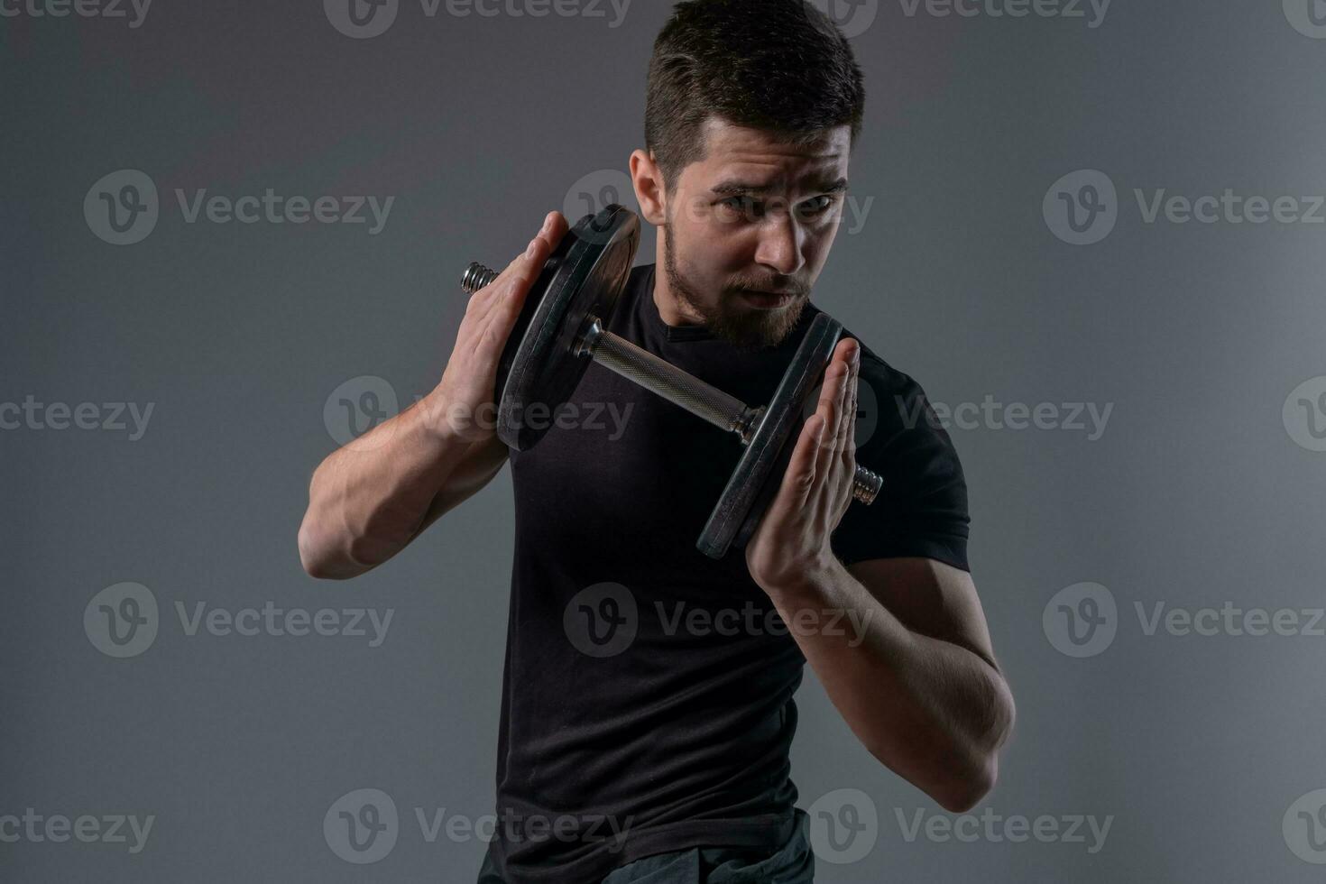 Young man with dumbbell in hands on grey background photo