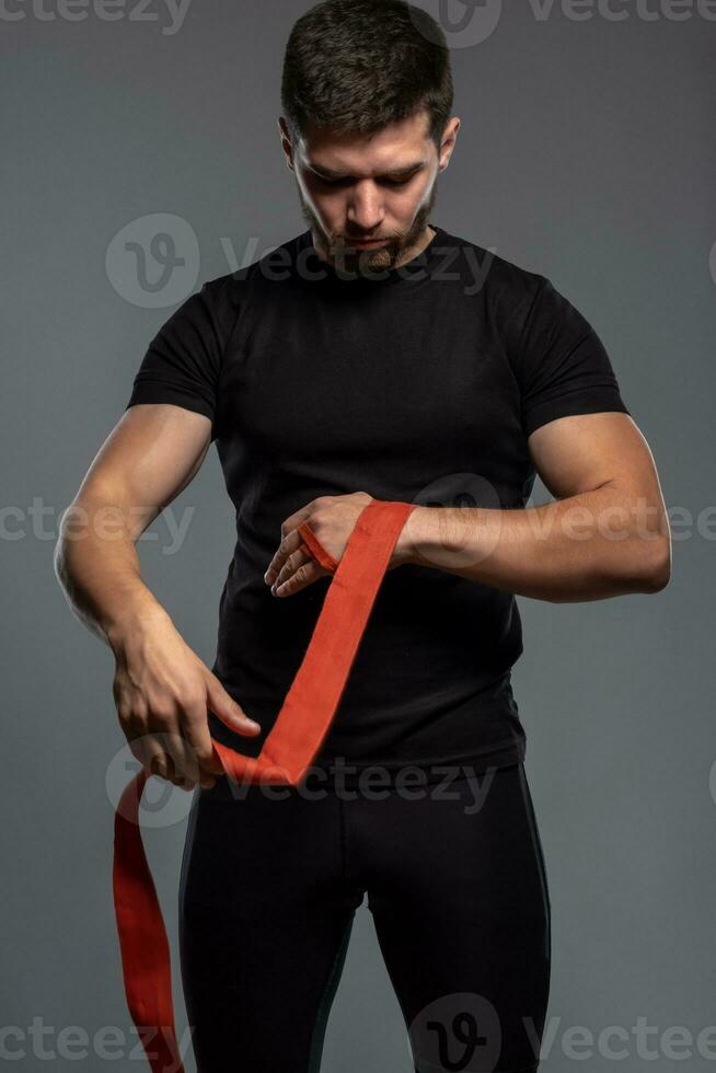 Focused guy wrapping hands with boxing tape before fight photo