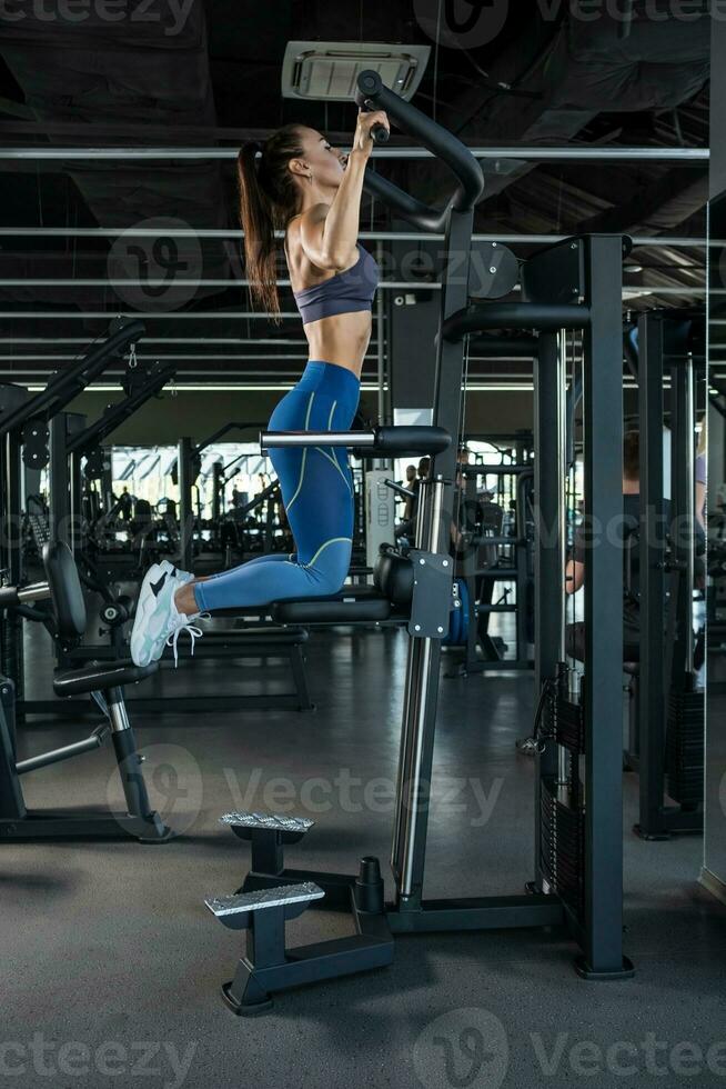 Sporty woman exercising on assisted pull-up machines at gym photo