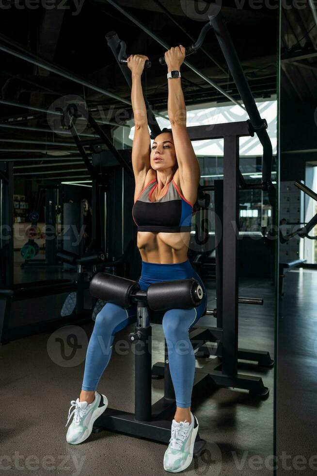 Girl doing reverse grip high lever row on strength machine at gym photo