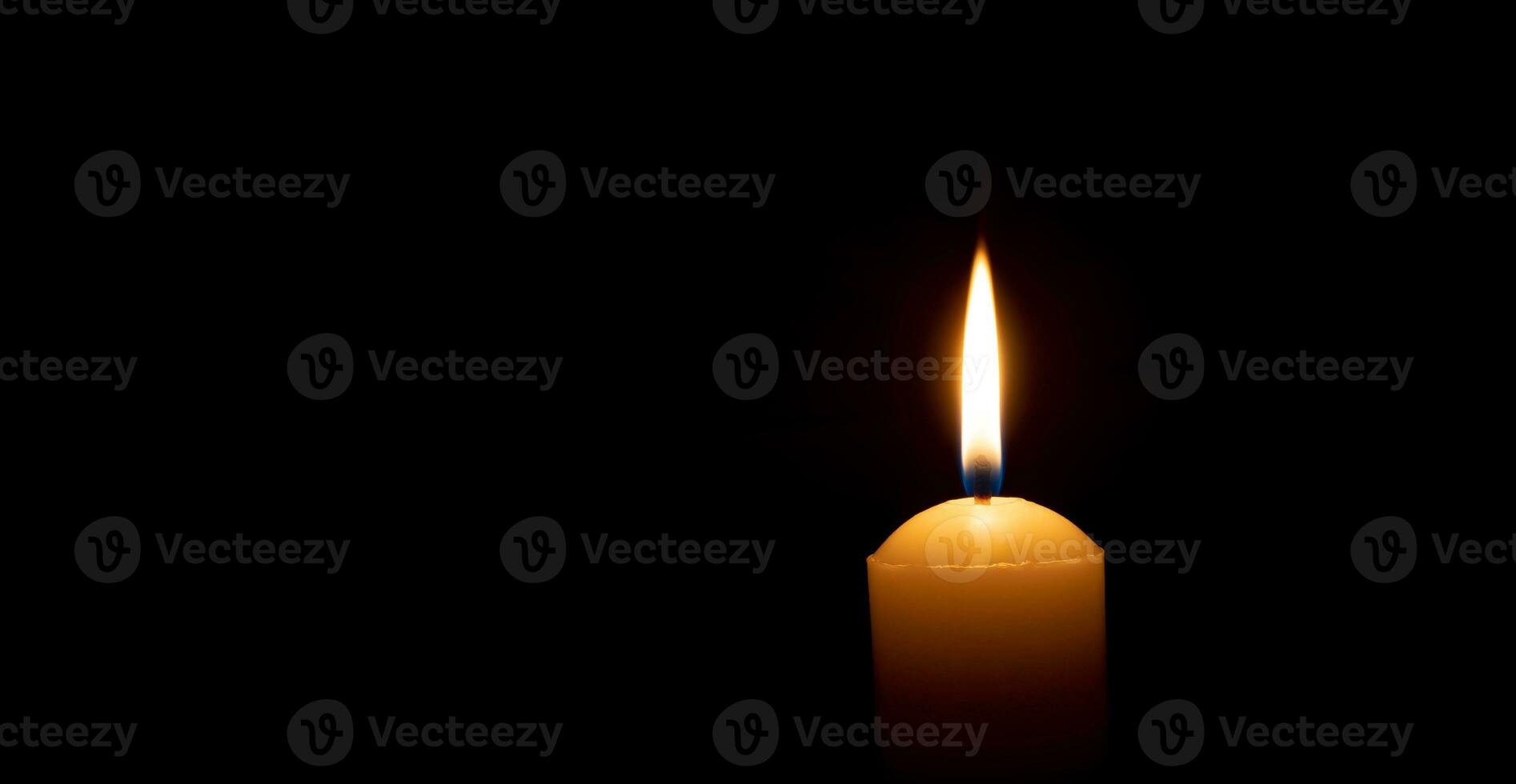 Single burning candle flame or light glowing on a big yellow candle on black or dark background on table in church for Christmas, funeral or memorial service with copy space photo