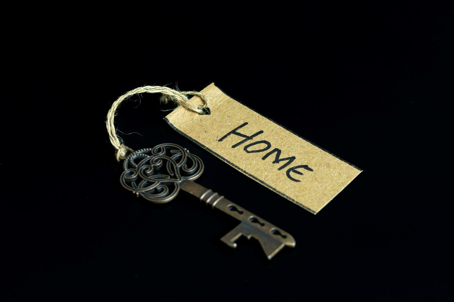Old decorative key and handwritten tag HOME tied with straw rope on black background photo