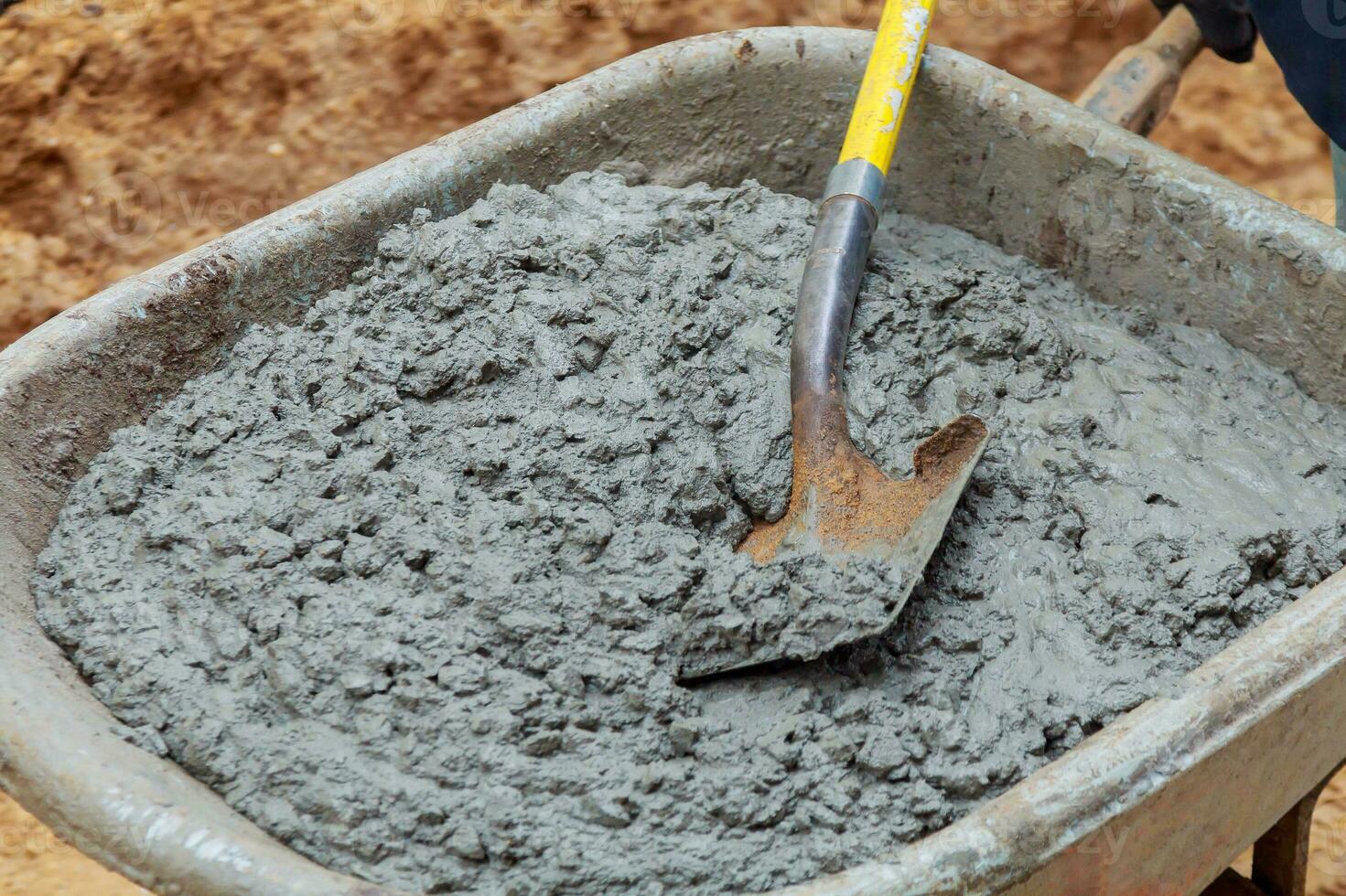 Worker shovels a wet mix of concrete from wheelbarrow at curb block installation. photo