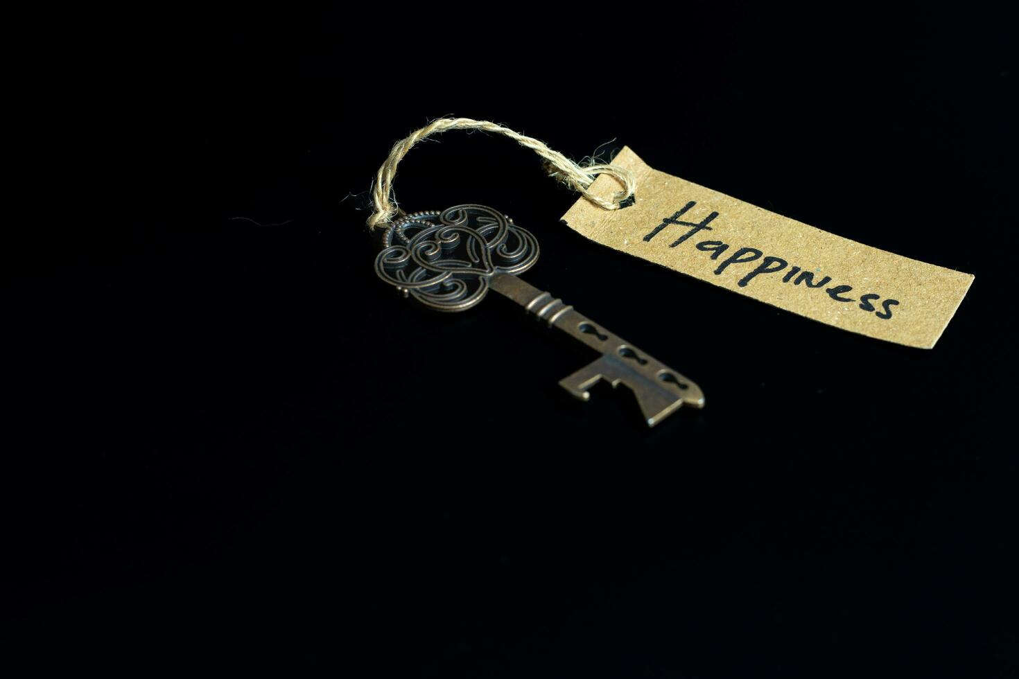 Old decorative key and handwritten tag Happiness tied with straw rope on black background photo