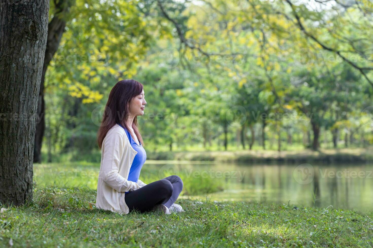 Woman relaxingly sitting and practicing meditation in the public park to attain happiness from inner peace wisdom under the tree in the summer photo