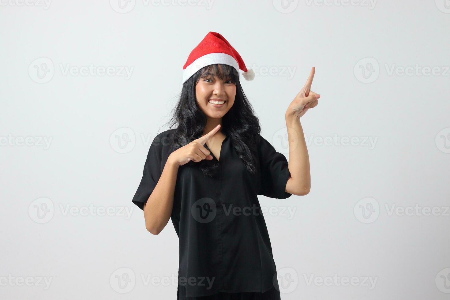 Portrait of attractive Asian woman with red Santa hat feeling happy, pointing and showing product to the side with finger. New year and christmas concept. Isolated image on white background photo