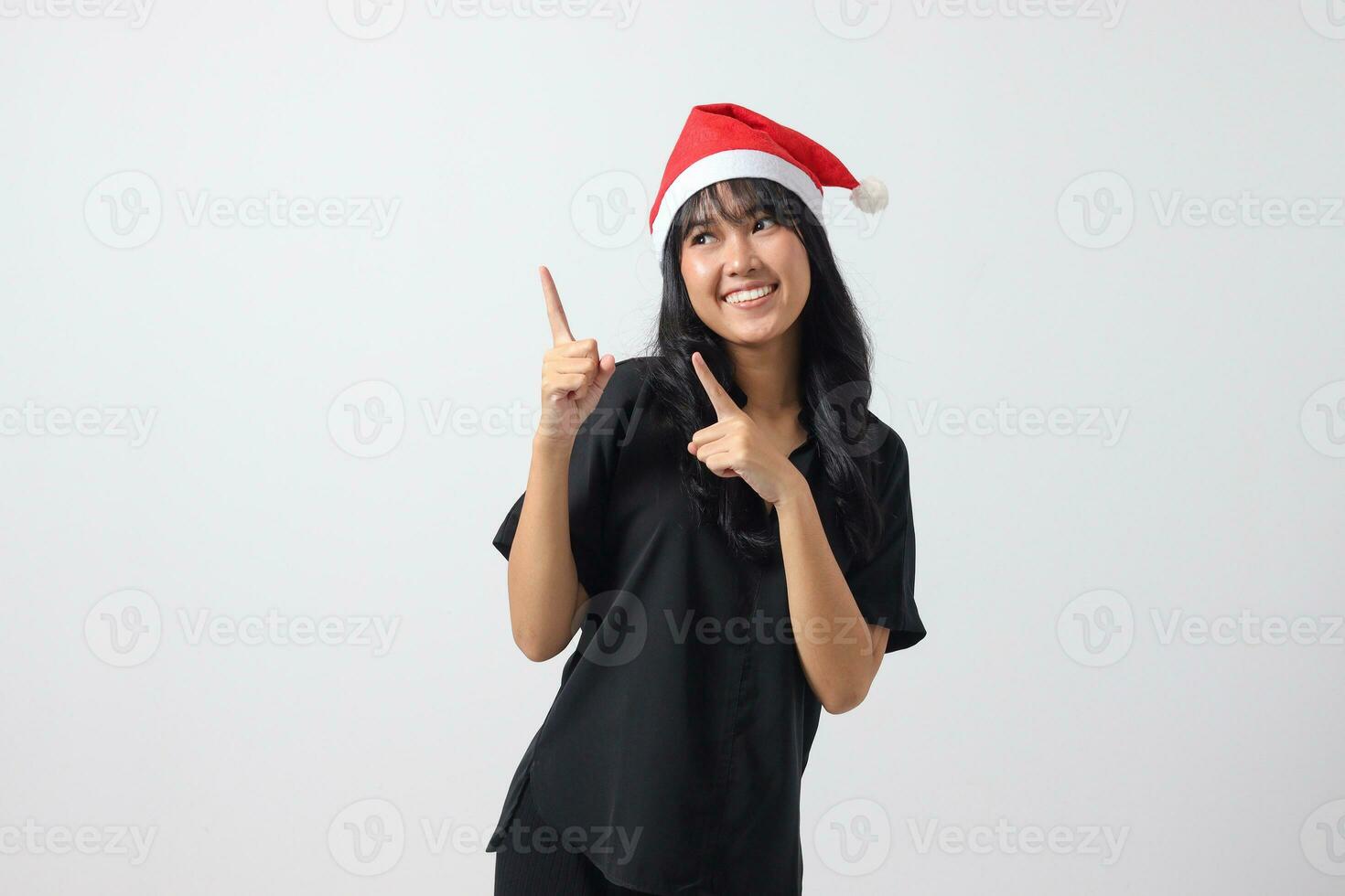 retrato de atractivo asiático mujer con rojo Papa Noel sombrero sensación feliz, señalando y demostración producto a el lado con dedo. nuevo año y Navidad concepto. aislado imagen en blanco antecedentes foto