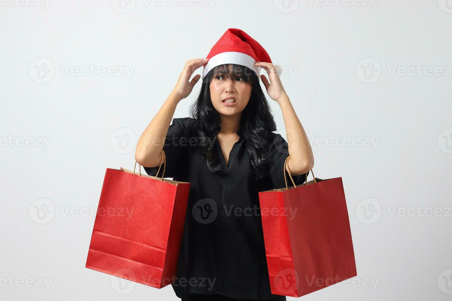 retrato de sorprendido asiático mujer con rojo Papa Noel sombrero sensación contento mientras adquisitivo cosa. emocionado niña participación compras bolsa. nuevo año y Navidad concepto. aislado imagen en blanco antecedentes foto