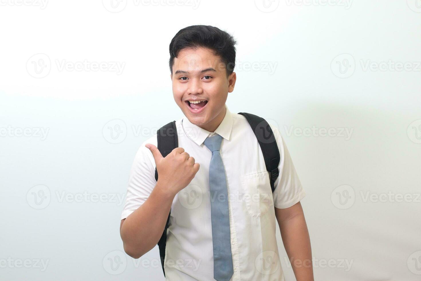 Indonesian senior high school student wearing white shirt uniform with gray tie showing product, pointing at something and smiling. Isolated image on white background photo